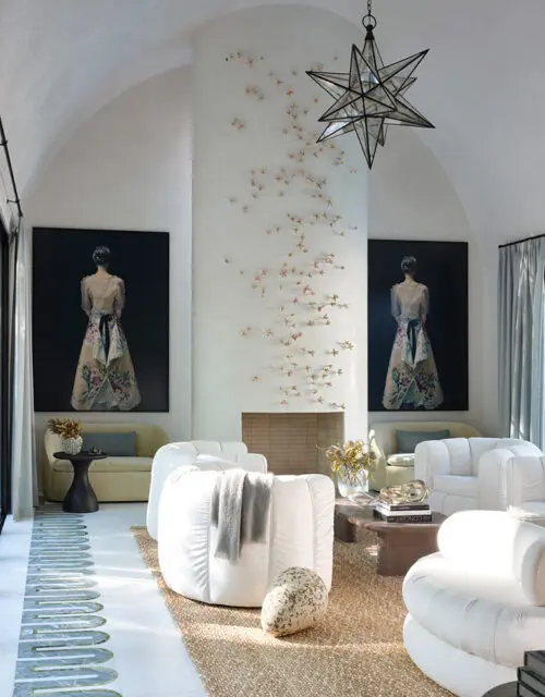 Living room with white curved sofas, fireplace with wall art, and starburst chandelier