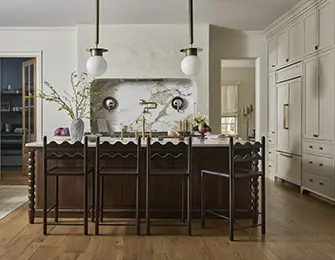 Kitchen island with dark wood base, marble backsplash, and brass faucet. Cream cabinetry and