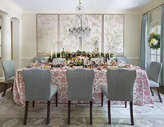 Dining room with a table set for a meal, floral tablecloth, light blue chairs, and three framed