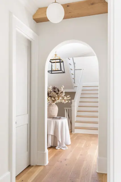 Hallway with arched doorway, white walls, wood floors, and staircase.
