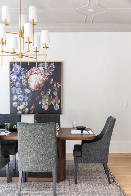 Dining room with dark floral painting, gold chandelier, and upholstered chairs.