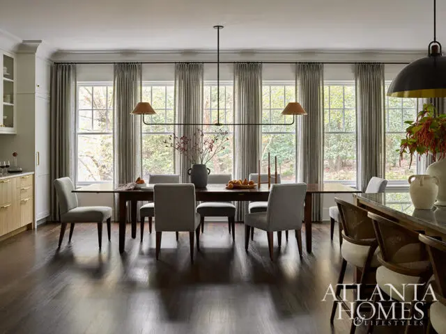 Dining room with dark wood table, upholstered chairs, and large windows with grey curtains.