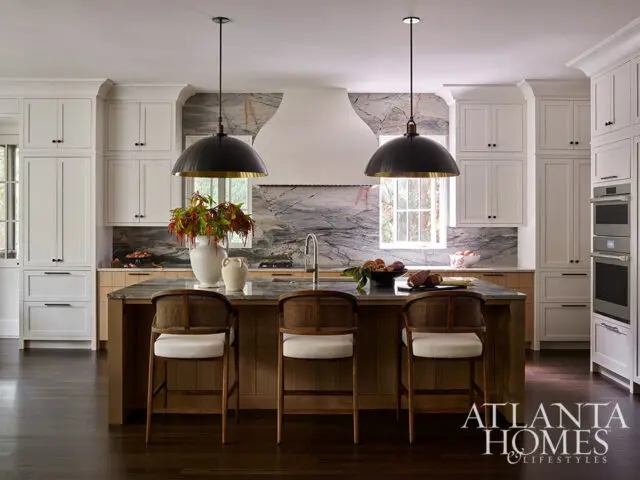 Kitchen with white cabinets, marble backsplash, and island with rattan stools.