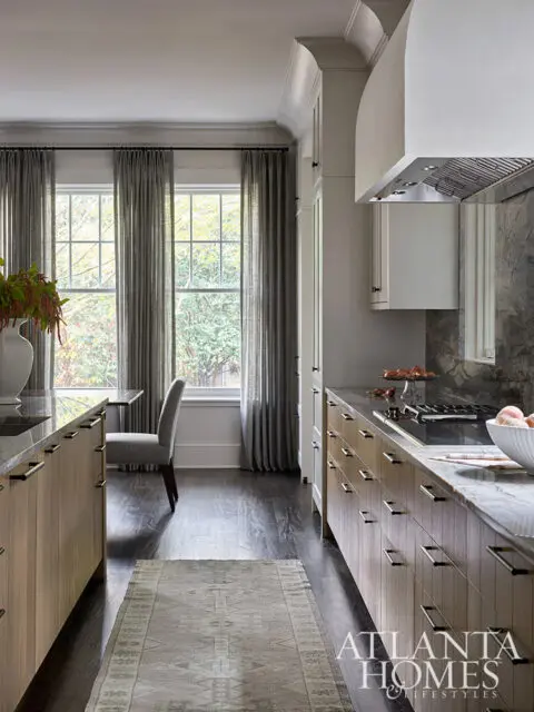 Kitchen with light wood cabinets, marble countertops, and dark wood floors. Gray curtains cover