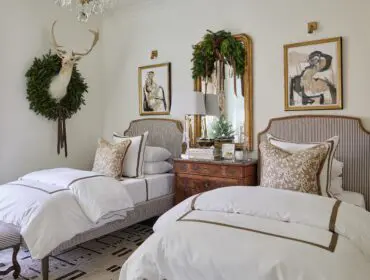 Bedroom with two twin beds, white bedding, striped headboards, and mounted deer head with wreath.