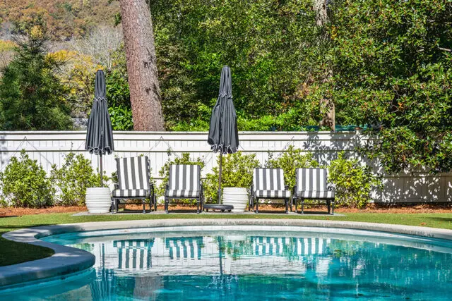 Four black and white striped lounge chairs with closed umbrellas by a pool