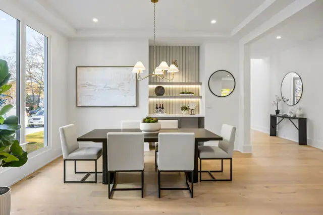 Dining room with dark wood table, white upholstered chairs, abstract art, and built-in shelves.