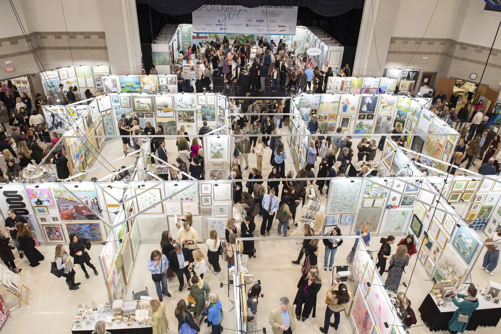 Crowded art fair with many booths displaying paintings and people browsing.
