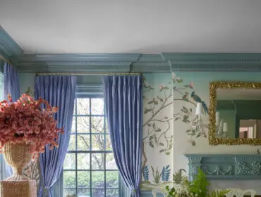 Dining room with blue curtains, floral wallpaper, and a wooden table set with dishes.