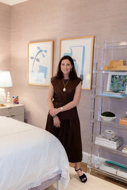 Woman in brown dress standing in bedroom with abstract art and acrylic shelves