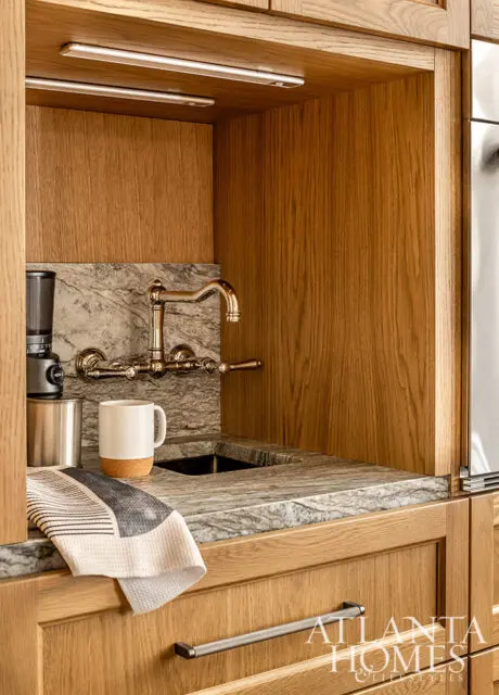 Wood paneled kitchen with marble countertop, brass faucet, and white mug.