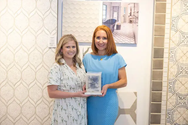 Two women holding an Atlanta Homes award, with decorative tiles on display.