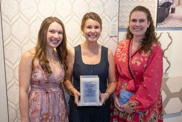 Three women smiling, one holding an Atlanta Homes award