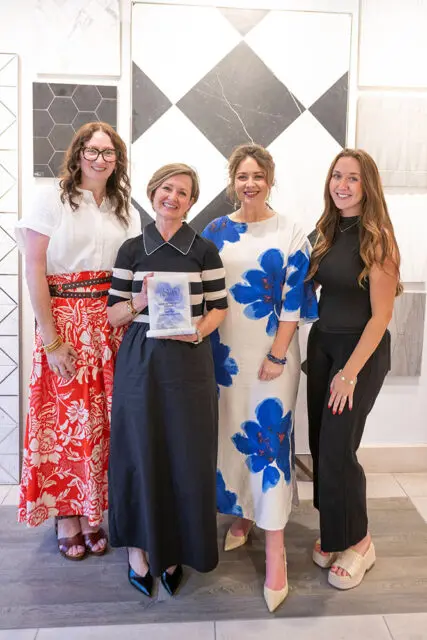 Four women stand in front of tile samples. One woman holds an award.