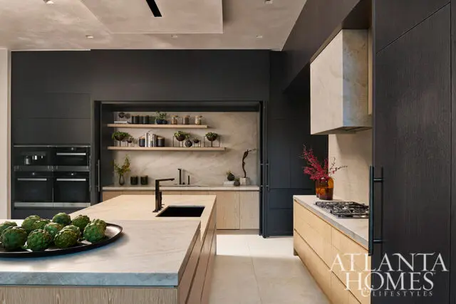 Modern kitchen with dark cabinetry, marble countertops, and light wood accents. Features built-in