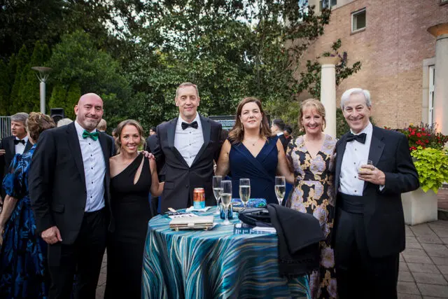 Group of six people in formal attire posing for a photo outdoors