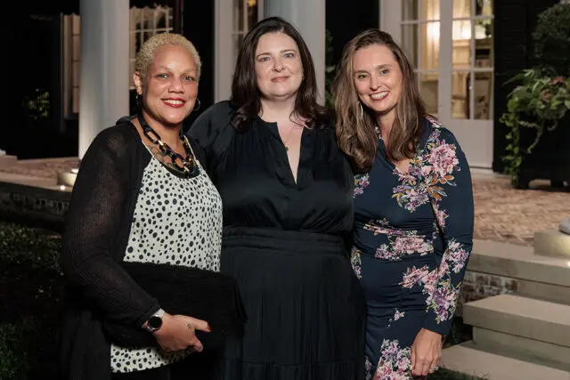 Three women posing outdoors in front of a building at night.