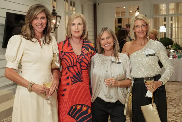 Four women holding drinks at an event. One woman wears a sequined top.