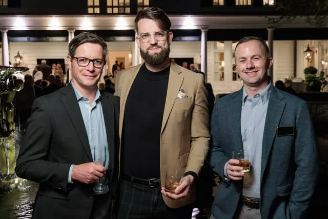 Three men in suits and blazers stand outside a building at night.