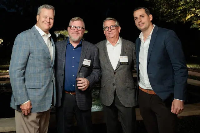 Four men in suits standing outdoors at night. Two men wear name tags that say SPONSOR.