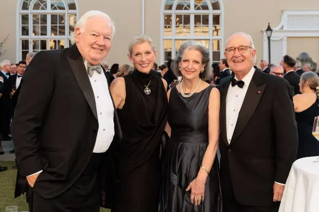 Four people in formal wear posing outdoors with a building in the background.