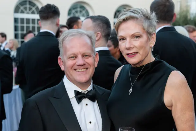 Man in tuxedo and woman in black dress smiling at camera