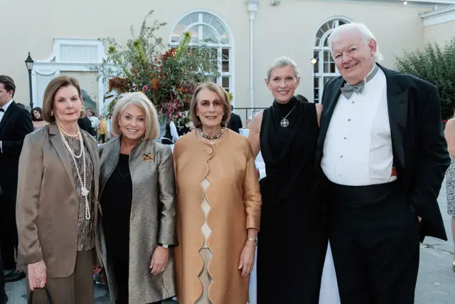 Five people posing for a photo outdoors. Two women in formal wear and pearls, two women in formal