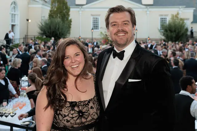 Man in tuxedo and woman in patterned dress smiling at event