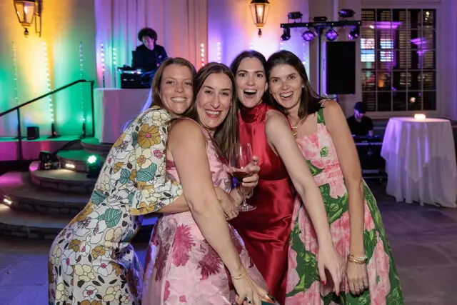 Four women posing for a photo at a party with a DJ in the background.