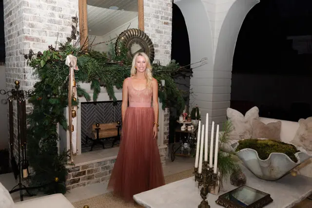 Woman in pink dress standing by a brick fireplace decorated with greenery