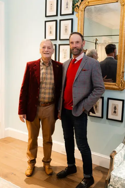 Two men posing in front of framed art and a large ornate mirror.