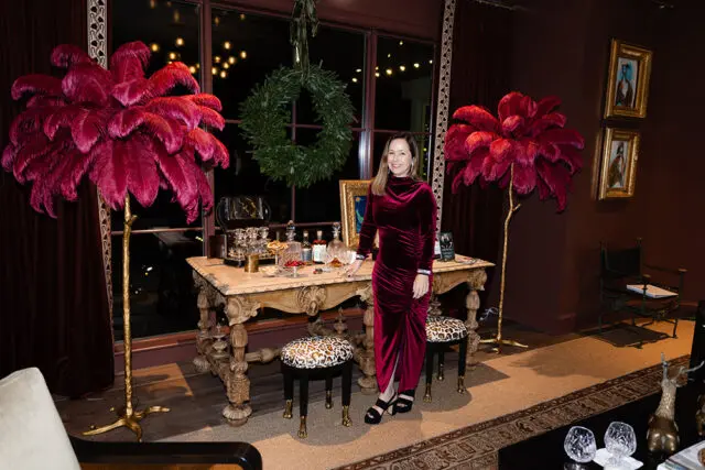 Woman in velvet dress by ornate table with barware and feather lamps.