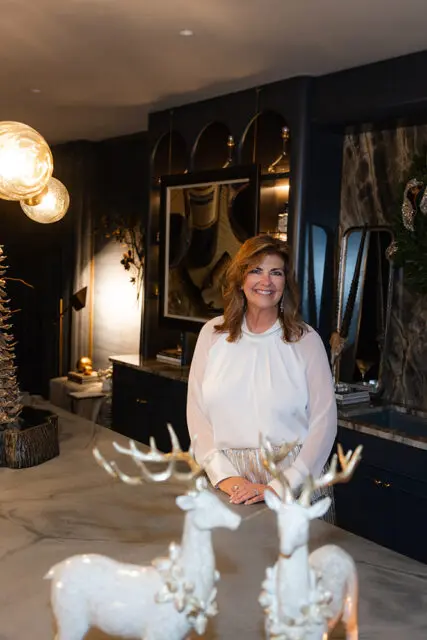 Woman in white blouse and silver skirt standing in a room with dark walls and decorative deer
