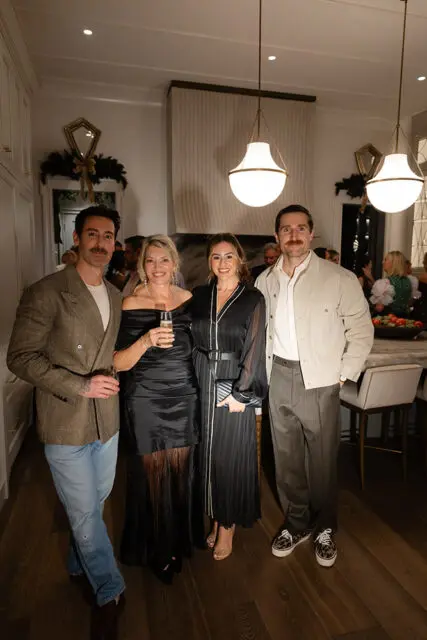 Four people posing in a modern dining room with pendant lights and holiday decorations.