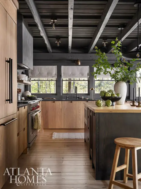 Rustic kitchen with wood cabinets, dark island, exposed beams, and stainless steel appliances.