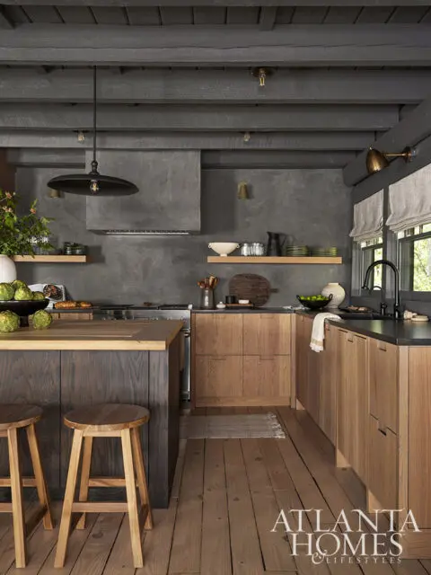 Rustic kitchen with dark wood island, light wood cabinets, concrete walls, and pendant light.