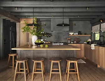 Rustic kitchen with wood island, four stools, dark gray walls, and exposed beams.
