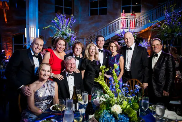 Group of people in formal attire posing for a photo at a formal event with floral arrangements.