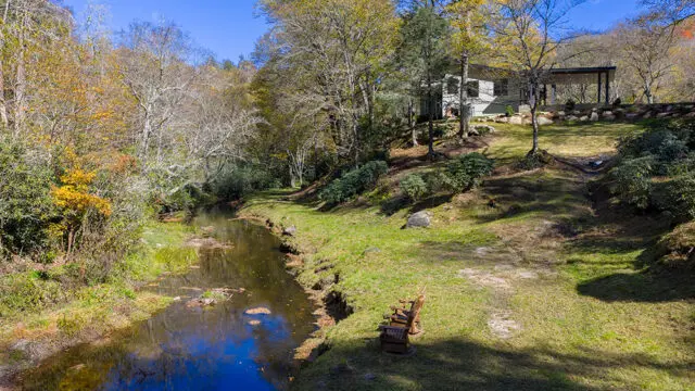 Modern house with light green siding and dark roof next to a stream in autumn