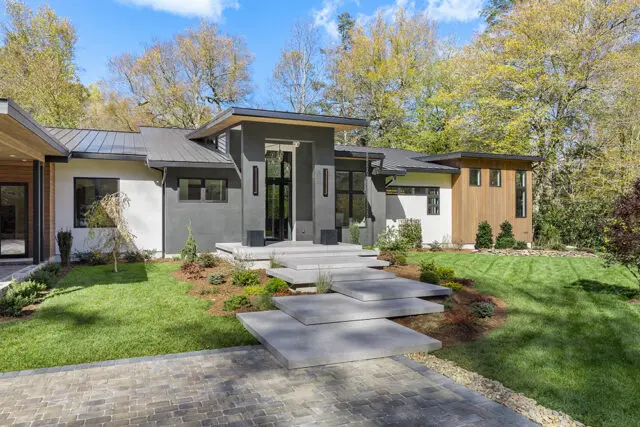 Modern home with gray stone facade, wood accents, and floating concrete steps.