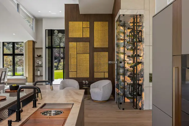 Modern kitchen with marble island, dark wood paneling, and glass wine cellar.
