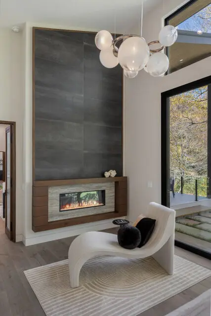 Living room with tall dark tile fireplace, chaise lounge, and modern chandelier