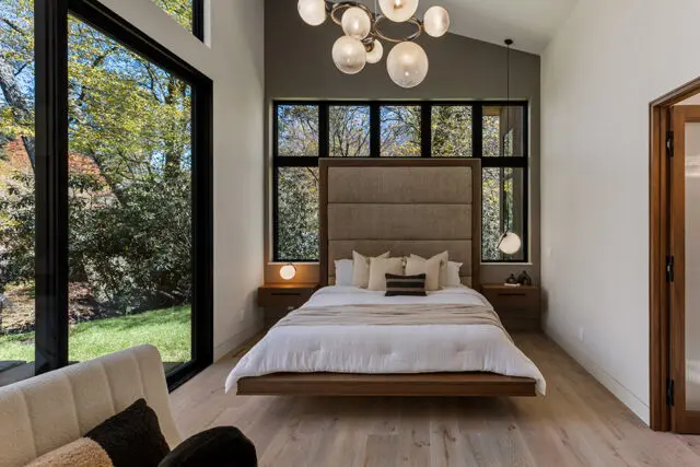 Bedroom with floating bed, upholstered headboard, and large windows overlooking trees.