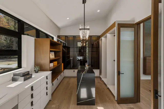 Walk-in closet with wood shelving, black marble island, and glass-fronted cabinets.