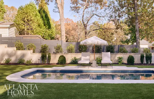 Curving pool with blue tile and white coping, two chairs and umbrella on lawn.