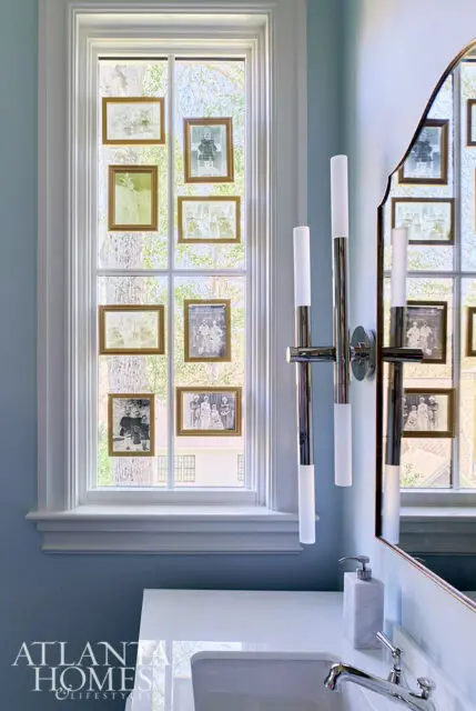 Light blue bathroom with window displaying framed vintage photos and a modern chrome sconce.