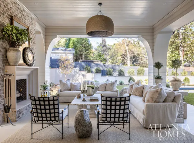 Covered patio with fireplace, neutral sofas, stone coffee table, and black chairs.