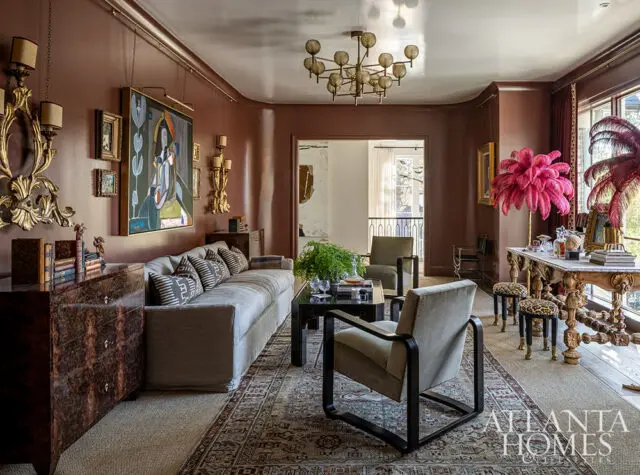 Living room with brown walls, gray sofa, patterned rug, and ornate table with pink feathers.