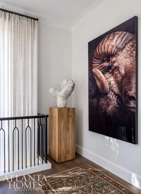 Hallway with large ram portrait, sculpture on wooden pedestal, and oriental rug