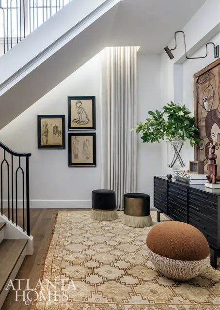Hallway with staircase, black console table, art, and stools on patterned rug.